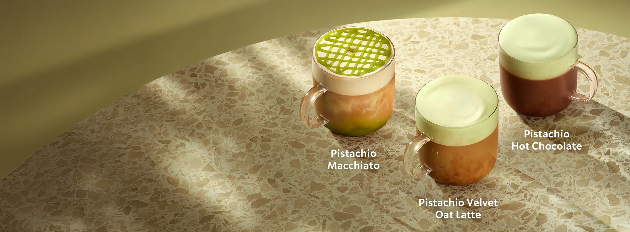 Three Starbucks drinks on a marble surface, each topped with green pistachio foam or drizzle.