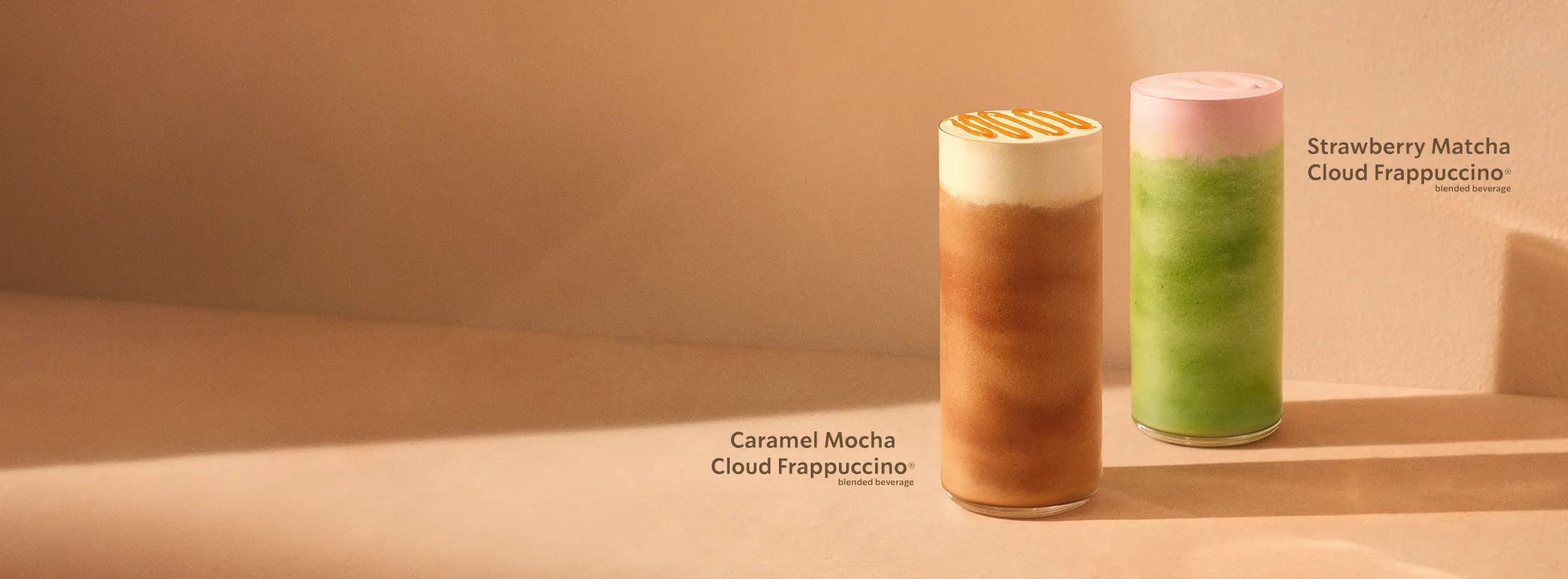Two tall blended Starbucks Cloud Frappuccino beverages on a warm beige surface. From left to right: a Caramel Mocha Cloud Frappuccino with a light foam top and caramel drizzleand a Strawberry Matcha Cloud Frappuccino with vibrant green blended matcha and a pale pink foam layer.