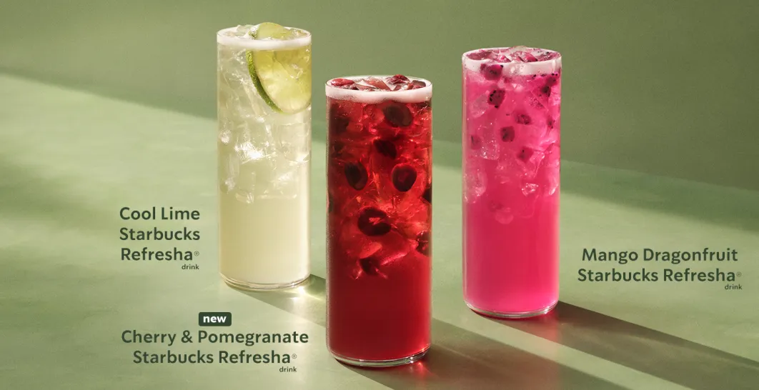 Three tall iced Starbucks Refresha beverages on a green surface. From left to right: a pale Cool Lime Refresha with lime slices, a deep red Cherry &amp; Pomegranate Refresha with fruit pieces, and a bright pink Mango Dragonfruit Refresha with visible ice and dragonfruit seeds.