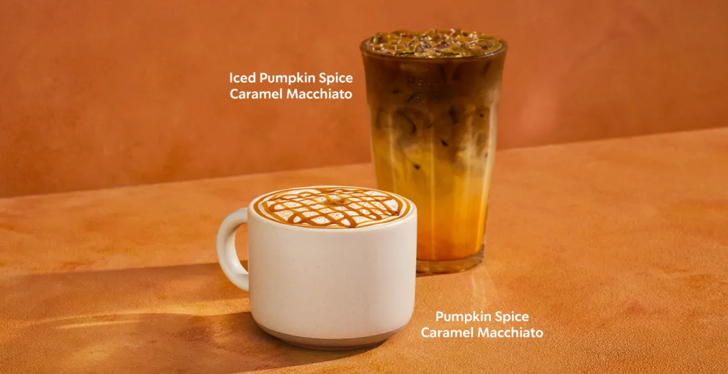 Two Starbucks pumpkin spice drinks on an orange background: a hot Pumpkin Spice Latte in a white mug topped with whipped cream, and an Iced Pumpkin Spice Latte in a clear glass filled with ice.