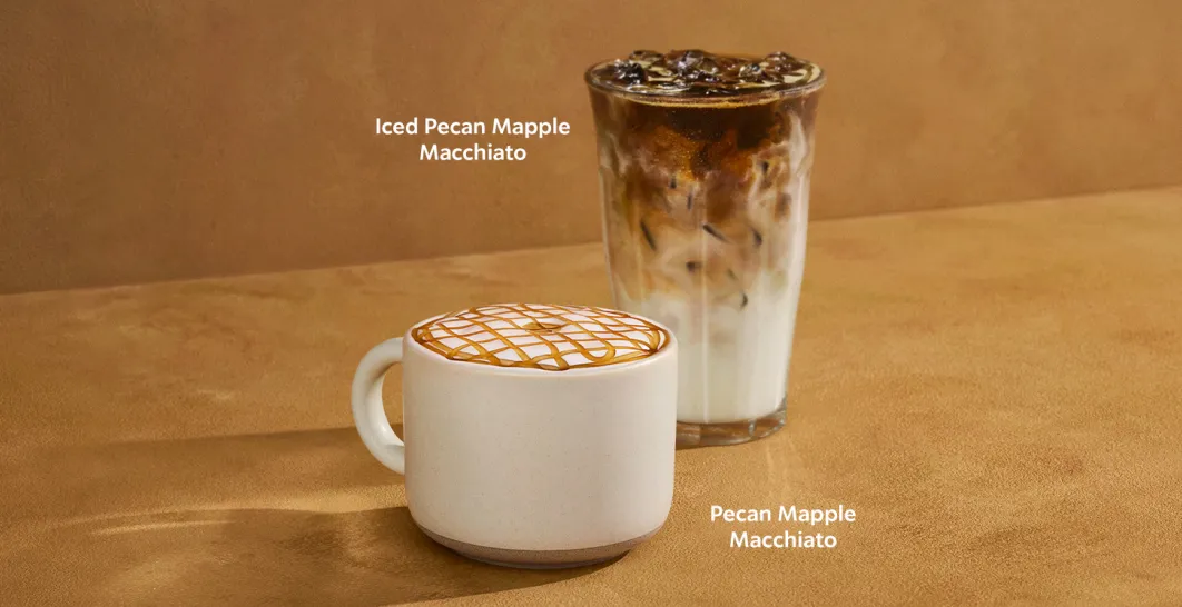 Two Starbucks Pecan Maple drinks on a brown background: a hot Pecan Maple Macchiato in a white mug topped with maple drizzle, and an Iced Pecan Maple Macchiato in a clear glass filled with ice.